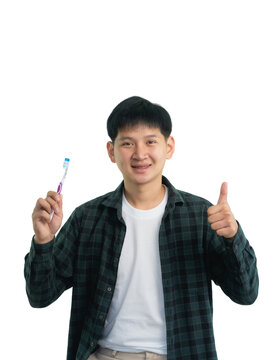 Asian man is holding a toothbrush and smiling. He is giving a thumbs up gesture. The image conveys the importance of dental hygiene and the positive attitude towards. Isolated on white background.