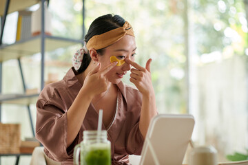Smiling woman applying eye patches to get rid of puffiness