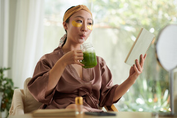 Young woman drinking morning smoothie and reading book