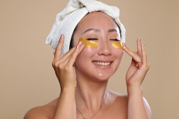Happy Chinese woman applying undereye patches after shower