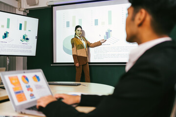 A cheerful and confident Asian businesswoman stands, presenting bar charts data from the projector...