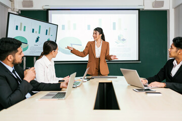 A cheerful and confident Asian businesswoman stands, present bar charts data from projector screen...