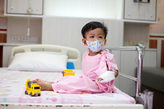 A 2-year-old child wearing a hospital gown was sick and was being treated in a hospital bed with toys.