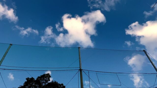 雲が流れる青空とグラウンドのネット