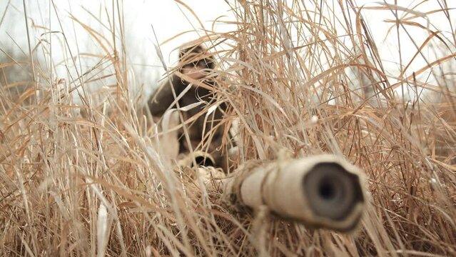 Camouflaged in thick, dry grass, a female sniper lies in wait, her intense focus channeled through the scope of her rifle as she zeroes in on the target. Camera 8K RAW.