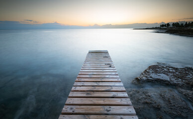 Long wooden pier in the sea at sunrise.