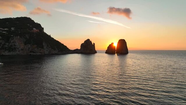 il sole spunta dietro I Faraglioni nel mare di Capri..
Ripresa aerea con drone dell'isola di Capri alle prime luci dell'alba. Sole giallo in una giornata estiva.