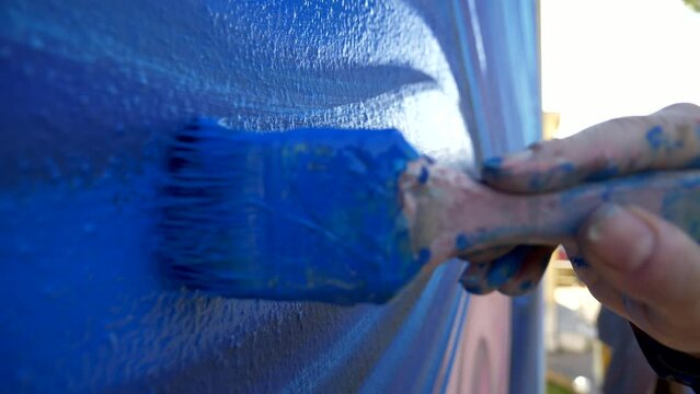 PENNELLO, VERNICE, COLERE BLU 24-0302Pittore dipinge una parete di colore blu. Primo piano sul pennello.
Ripresa al rallemtatore delle setole del pennello su un murals colorato di blu.