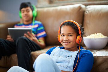 Tablet, children and portrait of girl with headphones in streaming, music or audio book with her brother at home. Kids, family and siblings in living room with digital, app or radio, relax or bonding