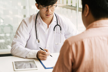 Asian doctor is examining the abnormal items of the body and diagnosing the disease in the paper with the medical report of the patient.