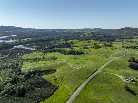 Drone image over beautiful green rolling hills in Northern California with New Hogan Lake in the background and a blue sky.