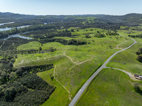 Drone image over beautiful green rolling hills in Northern California with New Hogan Lake in the background and a blue sky.