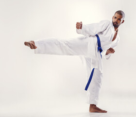 Man, kick and karate fighter in studio, fitness and martial arts on white background. Black male person, athlete and blue belt for taekwondo, discipline and warrior ready for self defense or battle