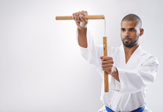 Nunchucks, karate and man in martial arts fight with weapon in training for defence in white background of studio. Nunchaku, exercise and fighting with equipment in sport with skill and power in club