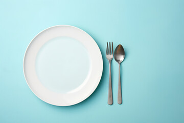 Minimalist Dining Concept with White Plate and Silverware Set on Pastel Blue Background, Top View of a Clean Table Setting