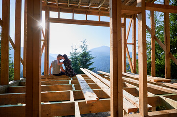 Man and woman inspecting their future wooden frame dwelling nestled in the mountains near forest....