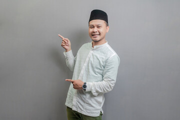 Happy asian muslim man recommend promo as pointing to copy space, indicate down link
