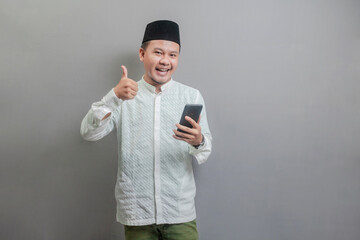 Asian Muslim man smilling and showing thumbs up and holding smartphone