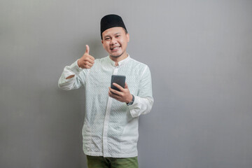 Asian Muslim man smilling and showing thumbs up and holding smartphone