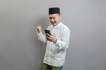 Asian Muslim man clenching his fist and looking his smartphone