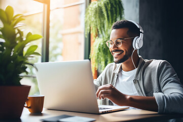 Cheerful Young Man Enjoying Music on Headphones While Working on Laptop in a Cozy Home Office Setting, Exemplifying Remote Work Flexibility and Lifestyle Balance