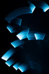 Blue neon curved wave of light as curls or swirl with smooth stripes on black background, pattern. Abstract background with motion light effect, light painting in contemporary style.