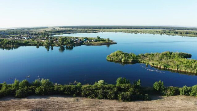 This stock video shows a beautiful lake, on the shore of which there is a settlement. This video will decorate your projects related to nature and summer landscapes.
