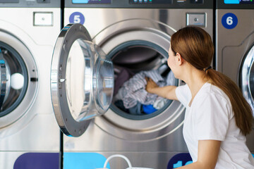 Asian female housewife bring used clothes to wash at self-service laundry shop.