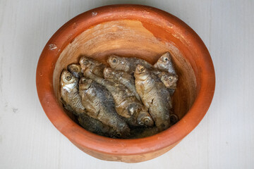Sun-dried Puti fish (Puntius) in an earthen pot on a brown textured background. Locally in Bangladesh, it is called Chepa Shutki. It is also known as pool barb, spotfin swamp barb, or stigma barb.