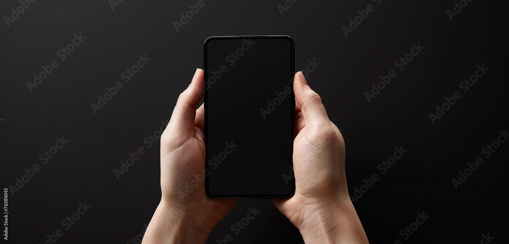 Wall mural Front view of a person holding a black screen mobile device, fingers poised to interact, against a pure black backdrop, illustrating simplicity and sophistication in modern gadgets - Wall murals