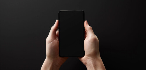 Obraz na płótnie Canvas Front view of a person holding a black screen mobile device, fingers poised to interact, against a pure black backdrop, illustrating simplicity and sophistication in modern gadgets