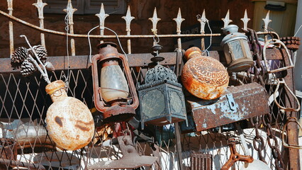 Collection of old utensils. Rust and peeling paint. Lanterns and flags are hanging on the fence. A...