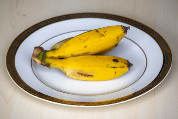 Yellow ripe bananas on a white plate serving for breakfast. The morning banana diet can help with weight loss, as bananas are rich in fiber that helps to keep you full. 