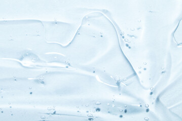 The smear of a transparent gel on a blue background. The texture of the skin or hair care product.