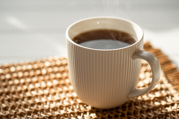 A steaming cup with a hot drink in the sunlight on the table. Morning tea or coffee.