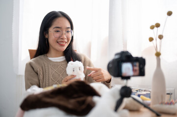 A cheerful young Asian female content creator showing her cute handmade plushie to the camera.