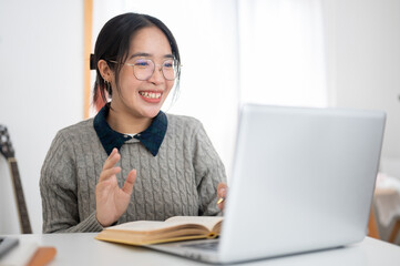 A cheerful young Asian female college student is studying online in a cafe co-working space.