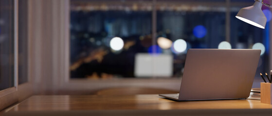 A laptop computer on a wooden desk in a contemporary room at night.