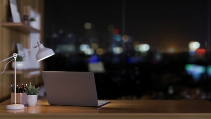 A laptop computer, a table lamp, and decor on a desk near the window with a nighttime view.