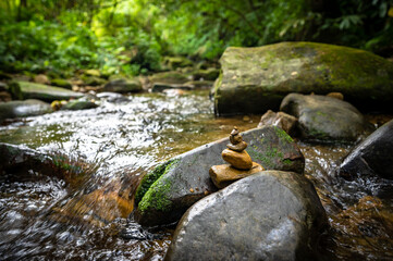 Little yellow rocks stacked on the river, hidden in the forest, next to the hiking trail,...