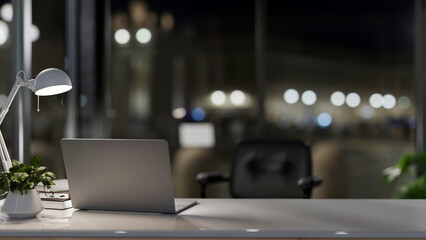 A laptop computer on a desk in a modern private office at night, illuminated by a table lamp. - obrazy, fototapety, plakaty