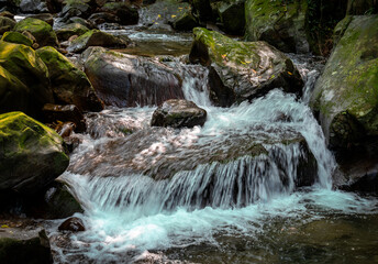 Beautiful river goes between rocks like a little waterfall, rocks full of green moss, and sunlight shines on it, in Nuandong Valley, Keelung city, Taiwan.