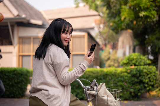 A beautiful, happy young Asian woman is using her smartphone while riding a bike in the city.