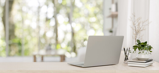 A back view image of a laptop on a wooden desk in a minimalist bright living room. - obrazy, fototapety, plakaty
