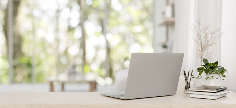 A back view image of a laptop on a wooden desk in a minimalist bright living room. - Powered by Adobe