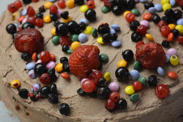 Bakery, homemade delicious pastries, sponge cake with brown cream sprinkled with bright colored candies with pieces of fruit.