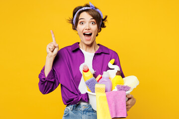 Young woman wear purple shirt hold basin with detergent bottles do housework tidy up hold index...