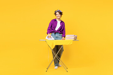 Full body young fun woman she wear purple shirt casual clothes do housework tidy up ironing clean clothes on board look camera isolated on plain yellow background studio portrait Housekeeping concept - obrazy, fototapety, plakaty