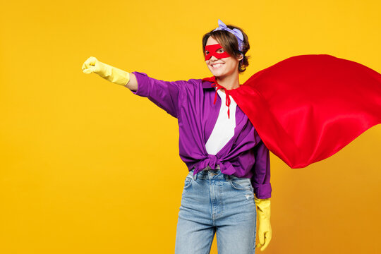 Side view young woman wears purple shirt rubber gloves super hero suit mask casual clothes do housework tidy up clench fist isolated on plain yellow background studio portrait. Housekeeping concept.