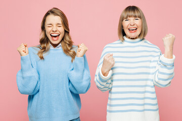 Elder happy excited parent mom 50s years old with young adult daughter two women together wear blue casual clothes do winner gesture isolated on plain pastel light pink background. Family day concept.